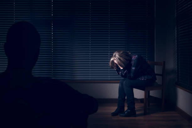 Regret A distraught woman with a head in her hands, while a man watches from the corner interrogation woman stock pictures, royalty-free photos & images