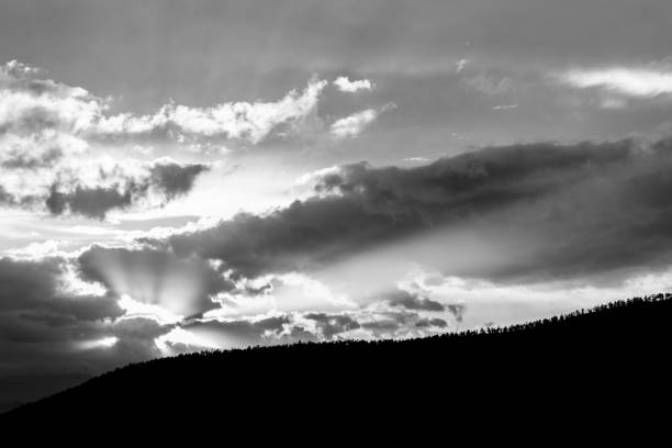 istock Sunset over a trees line on a hill, with sun rays coming out through some clouds 925631620