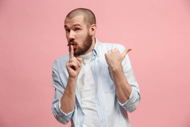 istock The young man whispering a secret behind her hand over pink background 925631972