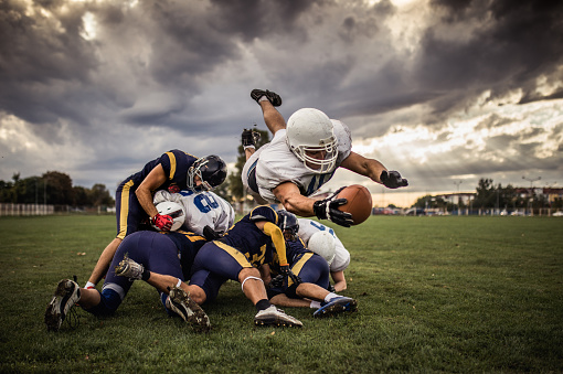 Determined American football player making a touchdown while passing through defensive players.