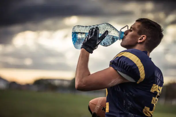 Profile view of young American football player drinking water on a break at playing field.