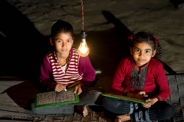 Rural girls studying in light bulb Two little Indian girls studying in single light bulb in the dark india poverty stock pictures, royalty-free photos & images
