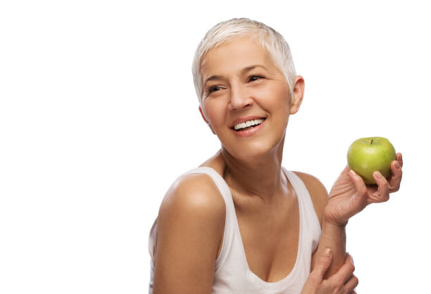 retrato de una hermosa mujer mayor sosteniendo una manzana, sonrisa, aislado sobre fondo blanco - apple women green eating fotografías e imágenes de stock
