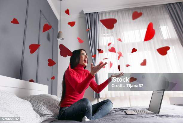 Beautiful Happy Young Woman Throwing Red Heartshapes In The Air Sitting On The Bed Stock Photo - Download Image Now