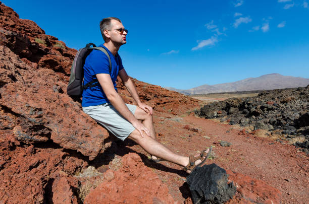 a sad tired man resting on a rock in a volcanic park of timanfaya - explorer tourist frowning men imagens e fotografias de stock