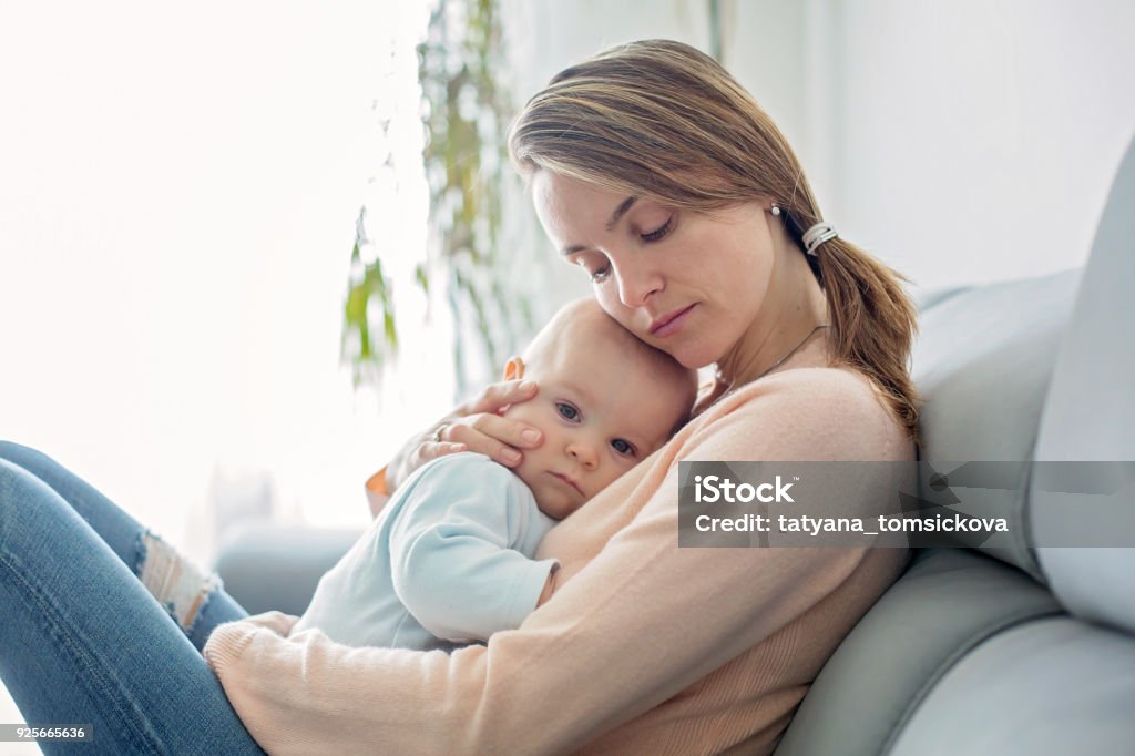 Giovane madre, tenendo il suo bambino malato, abbracciandolo a casa - Foto stock royalty-free di Bebé