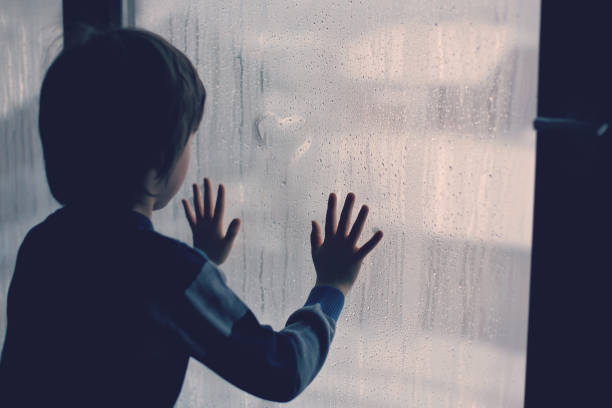 little boy, leaving finger prints and drawing hearts on a window - little boys child sadness depression imagens e fotografias de stock