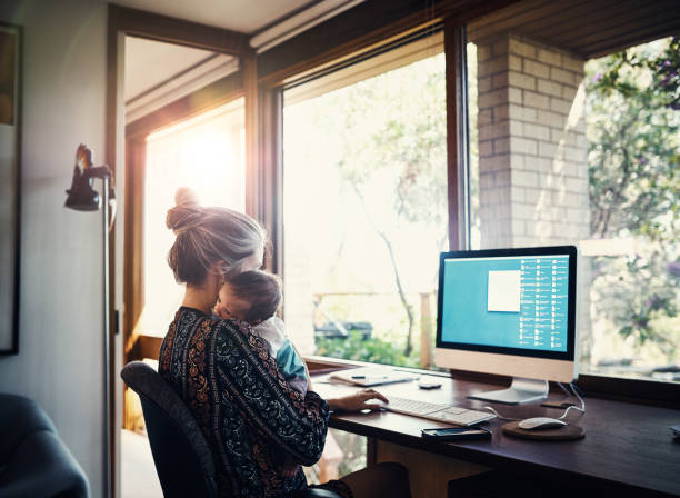 It’s not easy but she’s up to the task Shot of a young woman working at home while holding her newborn baby son working at home stock pictures, royalty-free photos & images