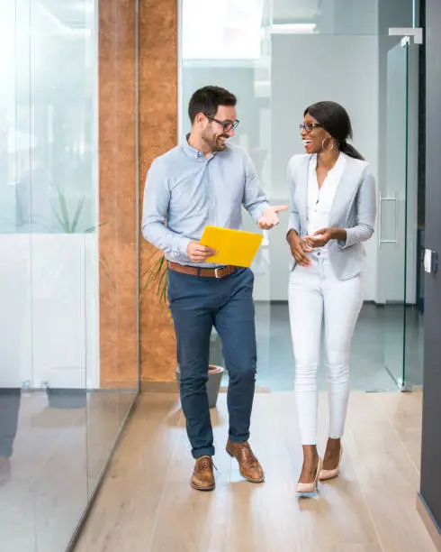 Photo of Two smiling business people walking through office hall and talking.