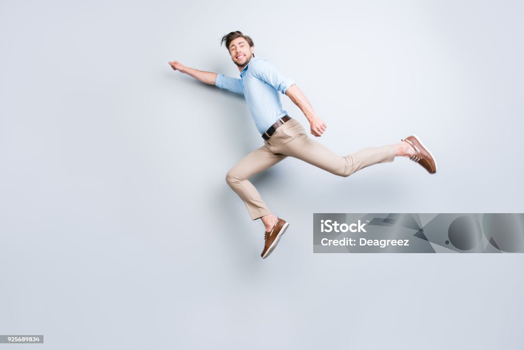 Happy, attractive, handsome, young man with bristle jumping in air showing superman pose looking at camera with beaming smile over grey background Flying Stock Photo