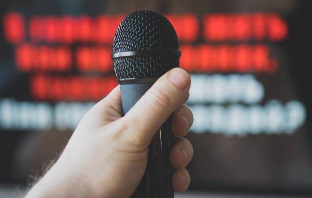 istock Man hand with karaoke microphone in front of TV. 925697670