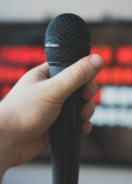 istock Man hand with karaoke microphone in front of TV. 925697696