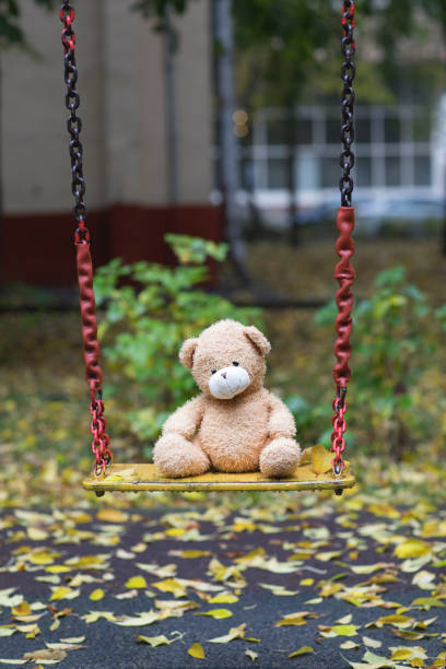 istock Brown plush teddy bear on a yellow colourful swing. 925698994