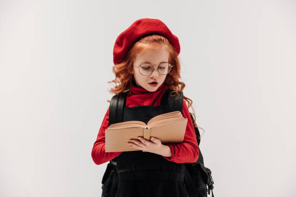 istock focused little schoolgirl reading book isolated on grey 925709608