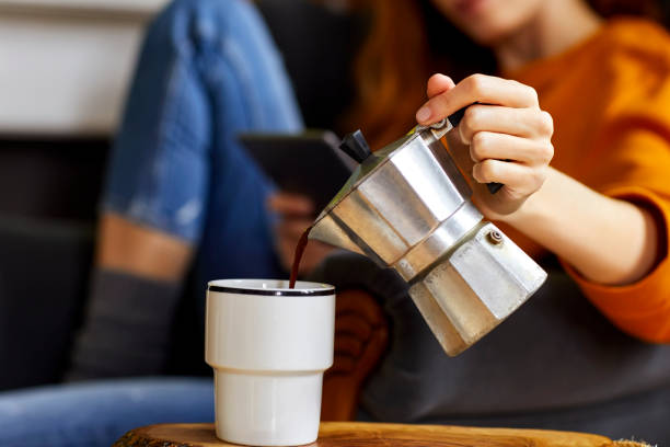 jovem mulher despejando café copa em casa - cup coffee pot coffee coffee cup - fotografias e filmes do acervo