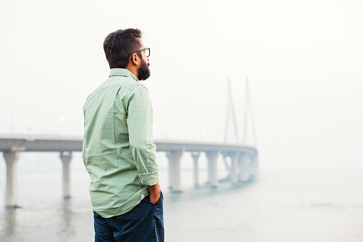 indian man standing and thinking in front of the bridge in mumbai