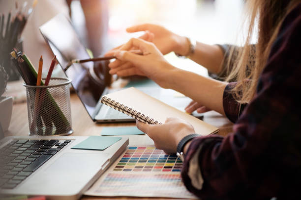 creative team deux femme travaillant avec l’ordinateur de bureau moderne, mains sélectives tenir bloc-notes papier. - styles photos et images de collection