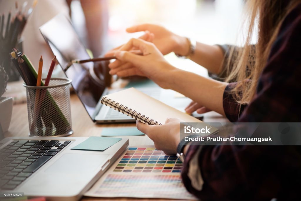 Creative team two woman working with computer in modern office, selective hands hold notebook paper. Marketing Stock Photo
