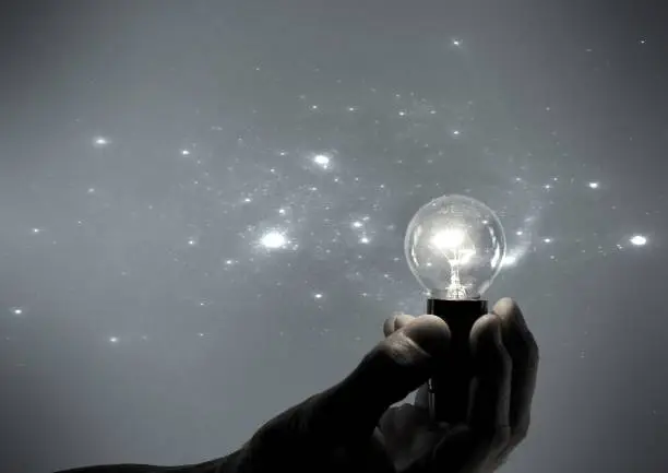 Male hand with incandescent light bulb and stars light effect on gray background.