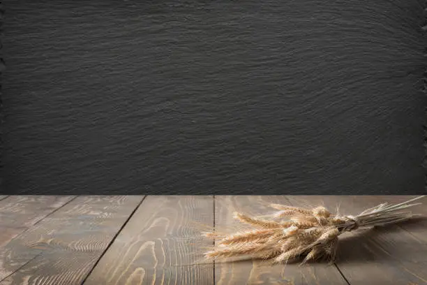 Photo of Kitchen abstract background. Wooden tabletop with ears of wheat and black slate chalkboard for display or montage.