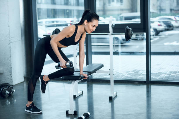 istock young sporty woman lifting dumbbell while leaning on workout bench at gym 925734586