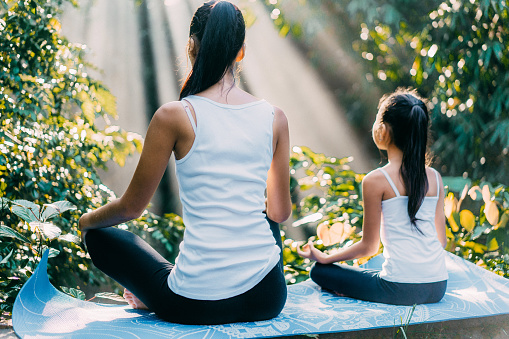 Asian mother  and daughter meditating in lotus position in rainforest in Bali, Indonesia