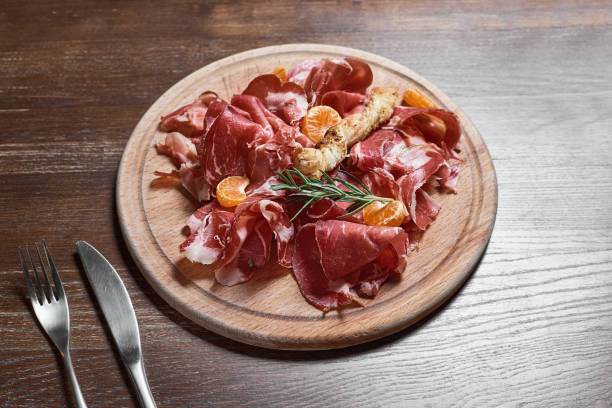 istock Wooden cutting board with prosciutto cheese on wooden table background. 925757784