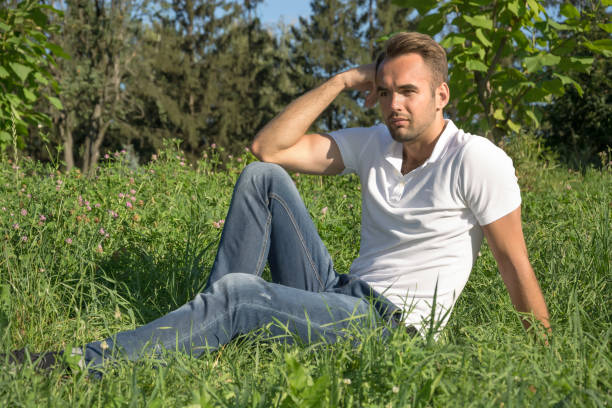istock Young man model looks sitting at tree in park 925770490