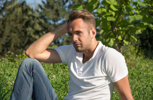 istock Young man model looks sitting at tree in park 925770608