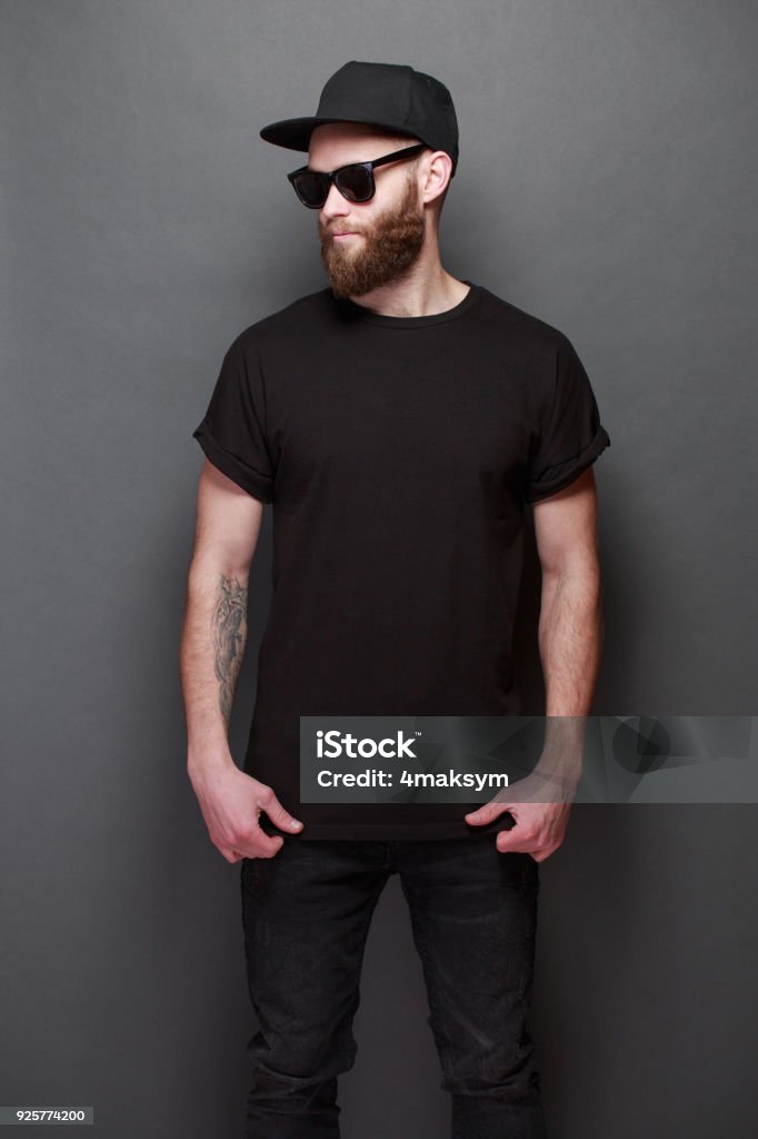 Hipster handsome male model with beard wearing black blank t-shirt with space for your logo or design over gray background T-Shirt Stock Photo