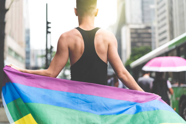 gay man holding rainbow flag - flag rainbow gay pride flag gay man imagens e fotografias de stock