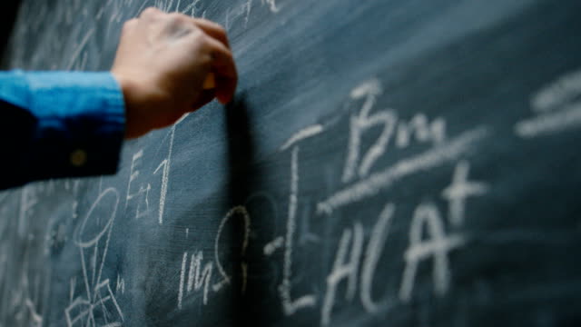 Hand Holding Chalk and Writing Complex and Sophisticated Mathematical Formula/ Equation on the Blackboard.
