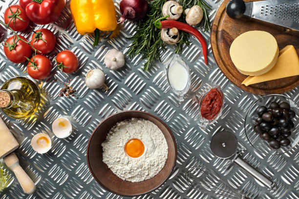 Ingredients and dough for making pizzas with an overhead view on freshly mixed mounds of pastry, a jar of olive oil and pot of tomato sauce, overhead view on metal background. Top view. Flat lay. Still life
