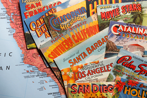 San Diego, CA, USA - February 27, 2018: A close up of several vintage postcards from the 1930's, 1940's and 1950's representing various cities and areas in California rest randomly on top of a map of California and photographed in a studio setting. Cities and areas represented include Santa Barbara, San Diego, Los Angeles, San Francisco, Catalina Island, Hollywood, and Palm Springs.  The postcards were a popular way for visitors and travelers to share their travel experiences with friends and family during the mid-20th century.