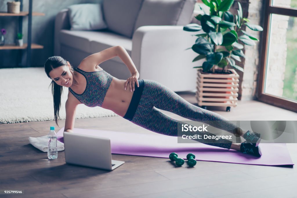 Beautiful sporty cheerful woman is doing side plank exercise. She is watching video on the internet and repeating the tasks Exercising Stock Photo