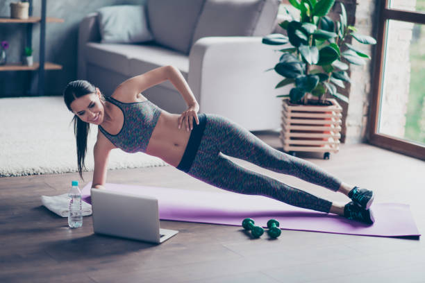 Beautiful sporty cheerful woman is doing side plank exercise. She is watching video on the internet and repeating the tasks Beautiful sporty cheerful woman is doing side plank exercise. She is watching video on the internet and repeating the tasks home workout stock pictures, royalty-free photos & images