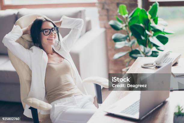 Photo libre de droit de Belle Indépendante Cute Femme En Costume Blanc Formelle Lunettes Assis Sur La Chaise À Son Bureau En Bureau Tenant Les Bras Derrière La Tête Avec Les Yeux Fermer À Penser Aux Vacances Vacances banque d'images et plus d'images libres de droit de Bureau - Lieu de travail