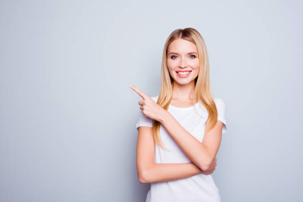 istock Pretty charming joyful confident calm friendly attractive blonde with shiny smile is pointing on empty space over her shoulder, isolated on grey background 925803786