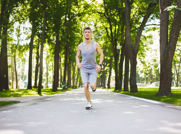 istock Young man running in green park, copy space 925820242