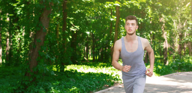 istock Young man running in green park, copy space 925820844