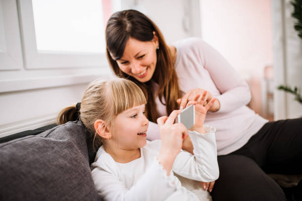istock Little girl using smart phone with her mother. Spending time together. 925831810