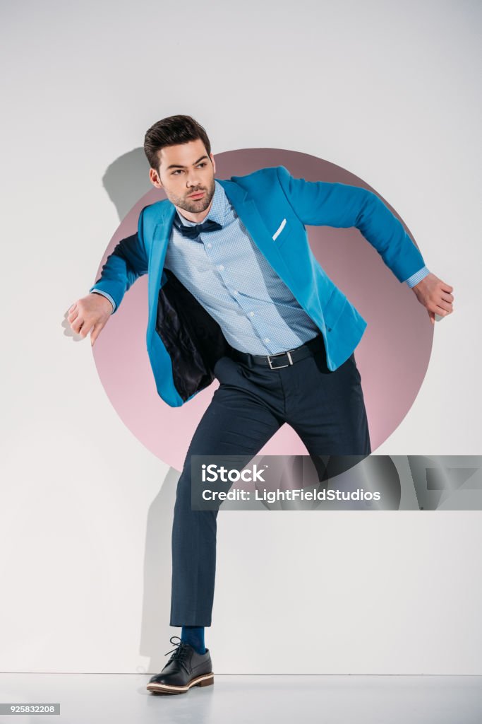 handsome stylish young man in suit and bow tie looking away while stepping through hole on grey Stepping Stock Photo