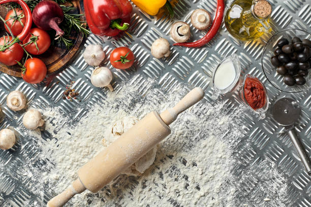 Ingredients and dough for making pizzas with an overhead view on freshly mixed mounds of pastry, a jar of olive oil and pot of tomato sauce, overhead view on metal background. Top view. Flat lay. Still life