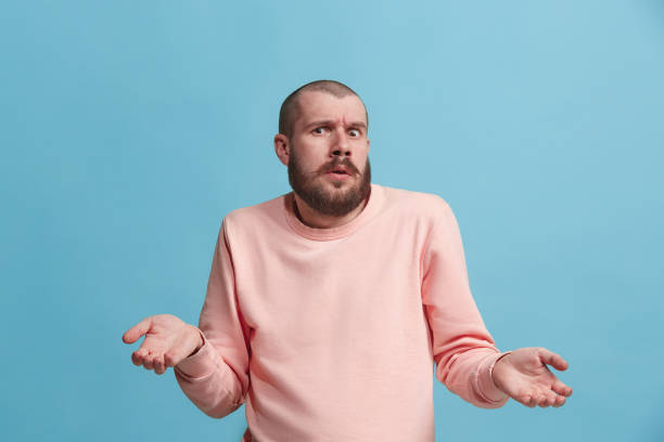 Beautiful man looking suprised and bewildered isolated on blue Why is that. Beautiful male half-length portrait isolated on trendy blue studio backgroud. Young emotional surprised, frustrated and bewildered man. Human emotions, facial expression concept. sad disbelief stock pictures, royalty-free photos & images