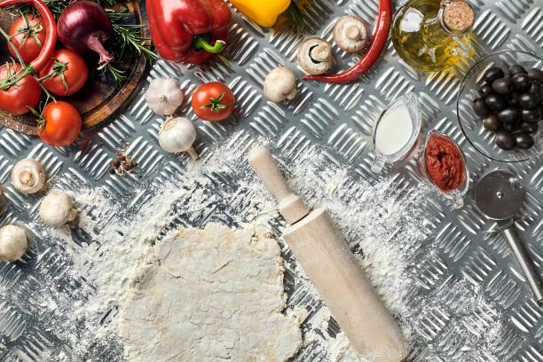 Ingredients and dough for making pizzas with an overhead view on freshly mixed mounds of pastry, a jar of olive oil and pot of tomato sauce, overhead view on metal background. Top view. Flat lay. Still life