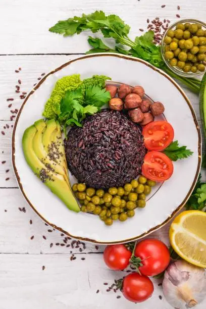 Healthy food. Black rice, avocado, cherry tomatoes, green peas and hazelnut. On a wooden background. Top view. Free space for your text.