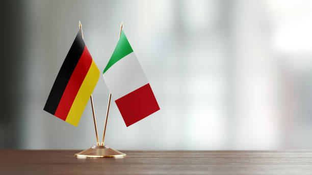 istock Italian And German Flag Pair On A Desk Over Defocused Background 925865806