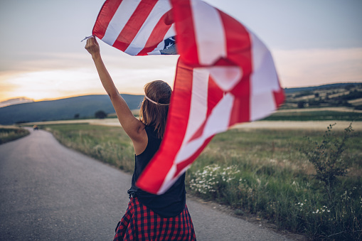 Young hipster woman walking on road with an American flag in her arms