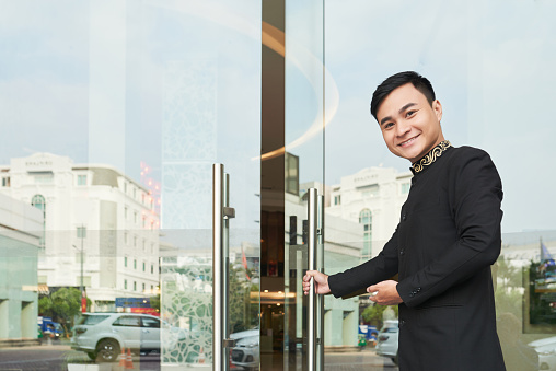 Cheerful Vietnamese hospitable server opening hotel door