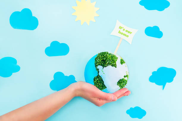 istock Female Hands holding Earth paper and green sprouts collage model with It's our home pointer on blue background with paper sun and clouds. Earth in your hands, Saving planet concept. 925898520